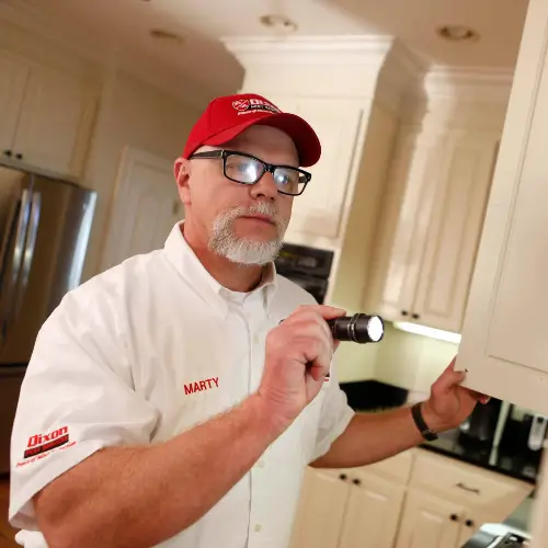 Pest control technician using a flashlight to look into cupboards